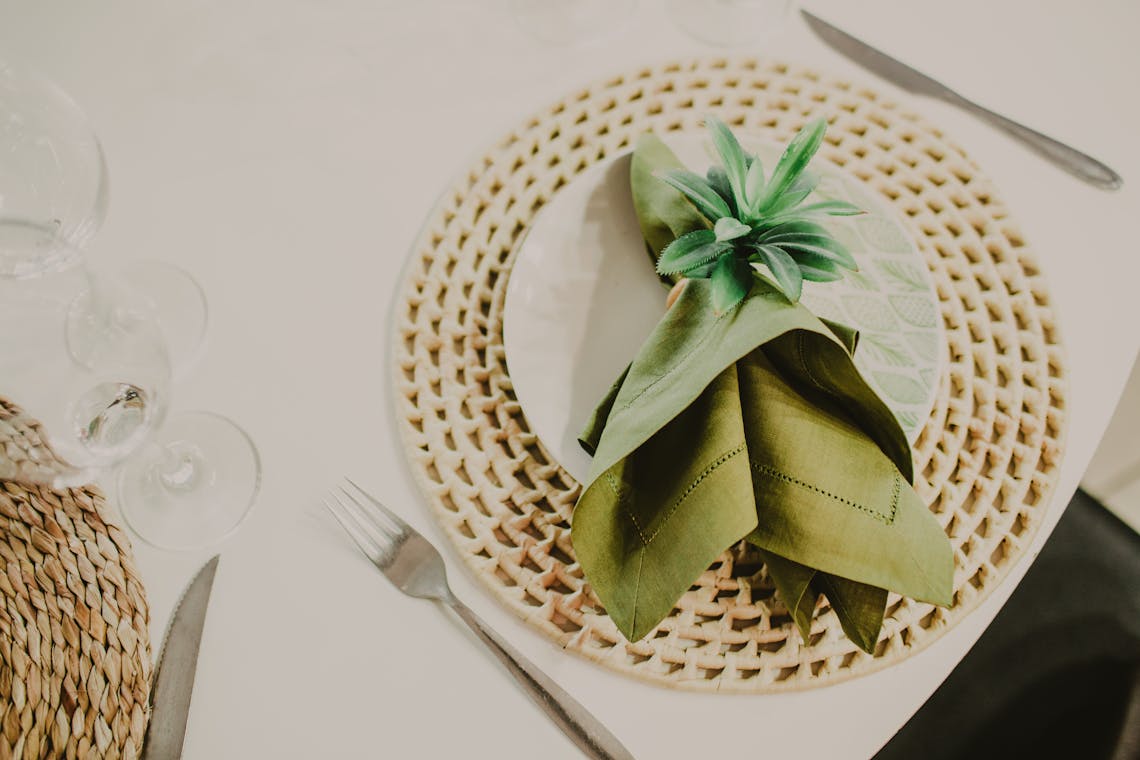 Chic table setting with woven mat, green napkin, and cutlery for a sophisticated dining experience.