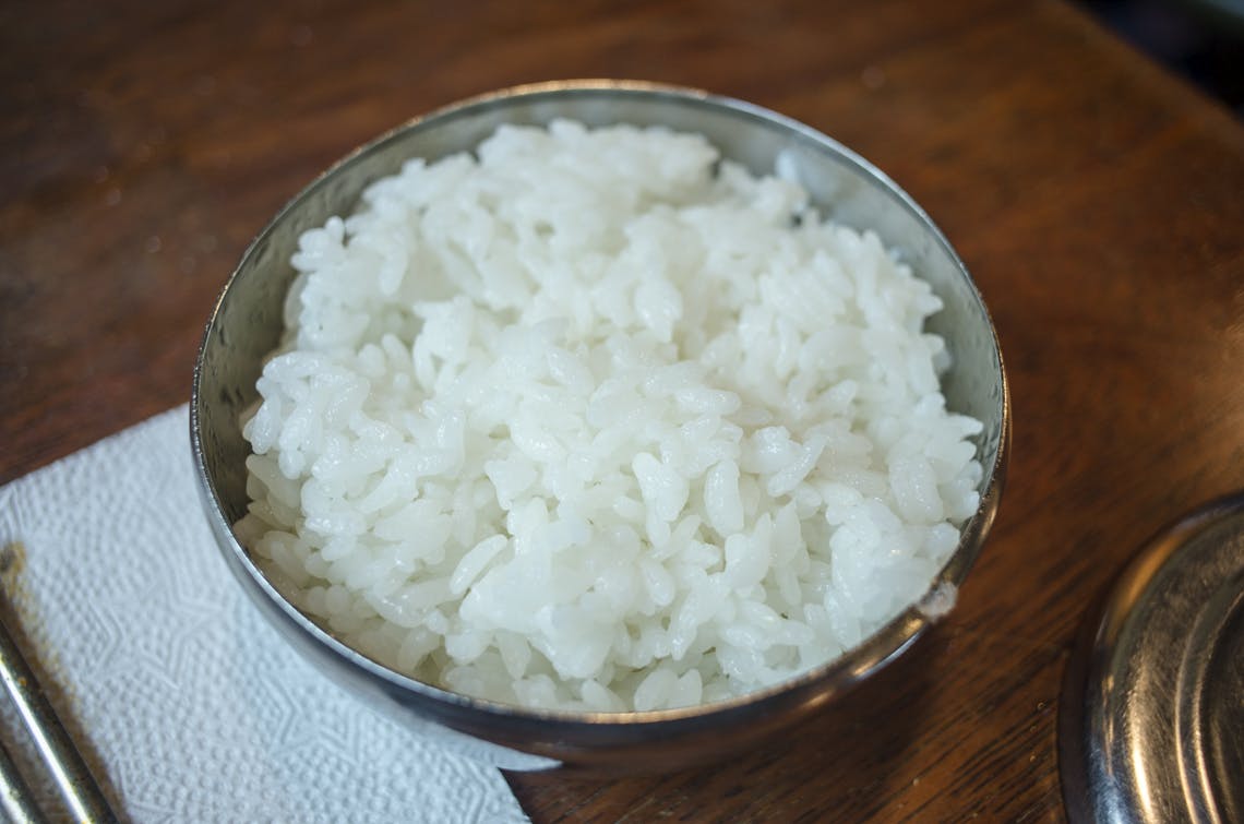 Close-up of steamed white rice in a stainless steel bowl on a wooden table.