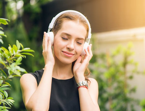 Smiling woman listening to music with headphones in sunny garden setting.