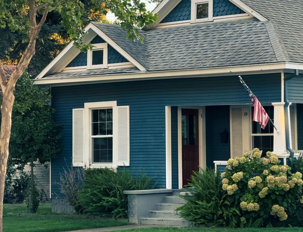 A picturesque blue cottage with a classic design, lush greenery, and a welcoming front porch.